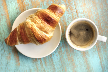 Cup of dark coffee with croissant, on wooden table