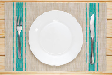 white plate with knife and fork on the tablecloth and wooden table