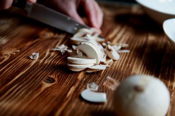 People cut mushrooms with a knife. The slices are adjacent. Wooden surface
