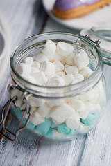 marshmallows in white and blue pastel colours on a light wooden surface. In a glass jar with a hinged lid