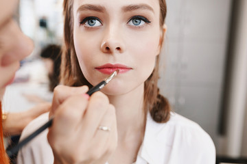 Closeup of female makeup artist paint her lips by cosmetic brush lipstick