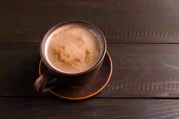 Hot chocolate or cocoa drink in clay cup, on dark brown wooden table