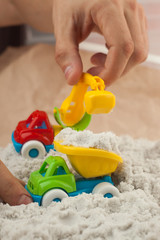 Man playing with kinetic sand and toy construction machinery. Hand of the man in the sand close up. Construction, mining, construction equipment at work