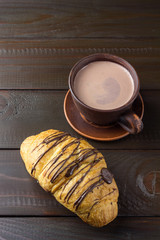 Hot chocolate or cocoa drink in clay cup and sweet croissant on dark brown wooden table