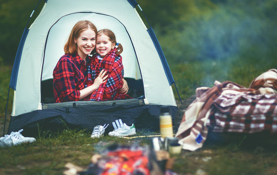 Family mother and child daughter drinking tea on a camping trip with a tent