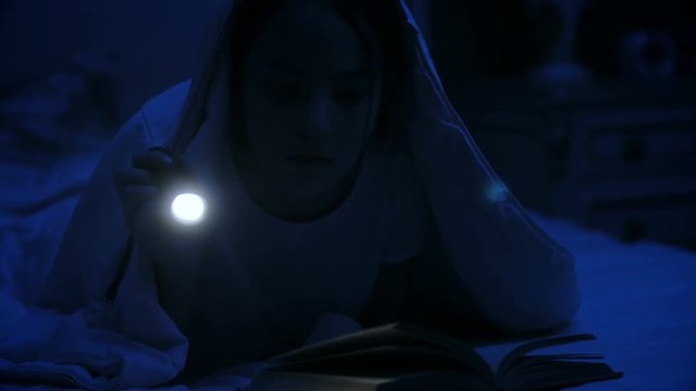4k video of girl with flashlight reading scary story under blanket at night
