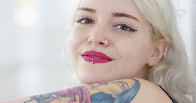 Beautiful pensive young modern hipster woman with shoulder length blond hair  a lip piercing and arm tattoo in a close up face portrait