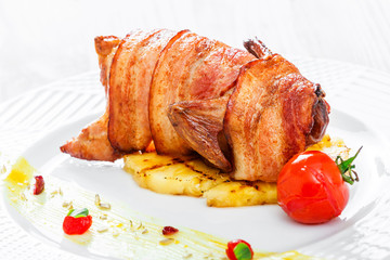Grilled chicken in a ham with pineapple and tomatoes on plate on wooden background close up. Hot Meat Dishes. Top view