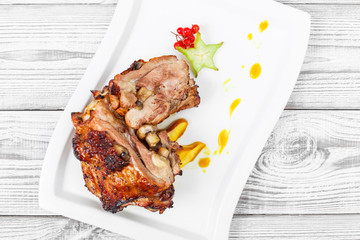 Roasted pork stuffed with mushrooms, peach, carambola, cranberries and sweet sauce on plate on wooden background close up