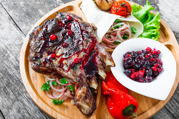 Grilled Ribeye Steak on bone with berry sauce, fresh salad and grilled vegetables on cutting board on wooden background close up