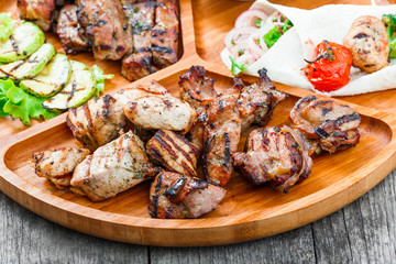 Assorted delicious grilled meat and vegetables with fresh salad and bbq sauce on cutting board on wooden background close up