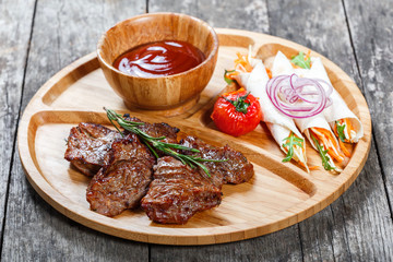 Grilled beef and vegetables with fresh salad and bbq sauce on cutting board on wooden background close up. Hot Meat Dishes