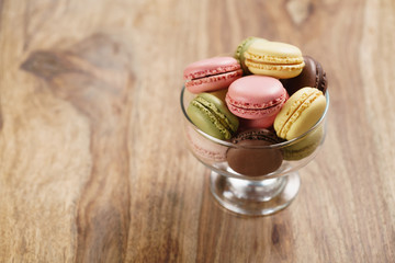 assorted macarons in glass bowl on wood table, with copy space