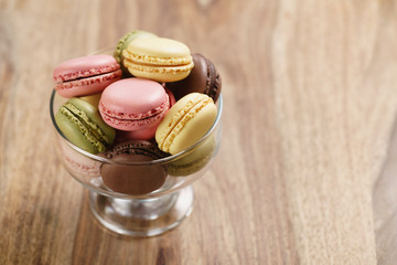 assorted macarons in glass bowl on wood table, with copy space