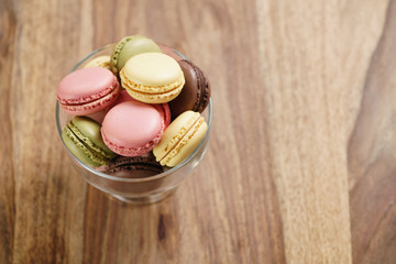 assorted macarons in glass bowl on wood table from above, with copy space