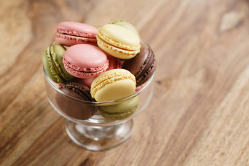 assorted macarons in glass bowl on wood table from above, with copy space