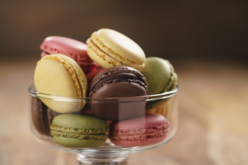 assorted macarons in glass bowl on wood table, closeup
