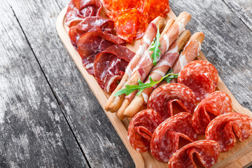 Antipasto platter cold meat plate with grissini bread sticks, prosciutto, slices ham, beef jerky, salami on cutting board