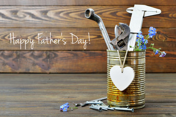 Happy Fathers Day card with tools, heart and flowers on wooden background