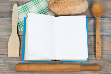 Open recipe book on wooden background, spoon, rolling pin , green checkered tablecloth.