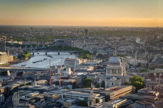 Stunning aerial view of St. Paul Cathedral, the city skyline and the river Thames against the evening orange sky at dusk in London, England, UK
