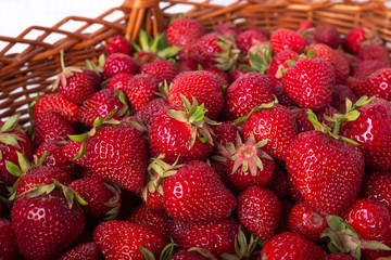 Wicker basket filled with ripe strawberries. On a white wooden background. Close-up.