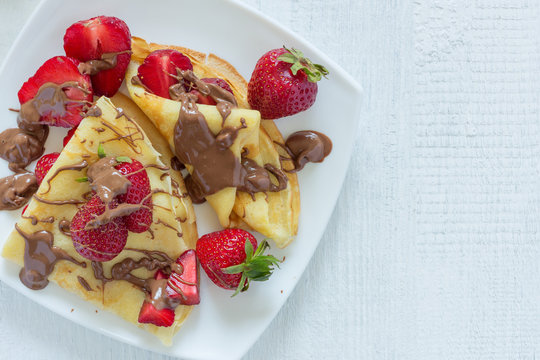 Pancakes with strawberries drizzled with chocolate. On a white wooden background. The view from the top. Copy-space.