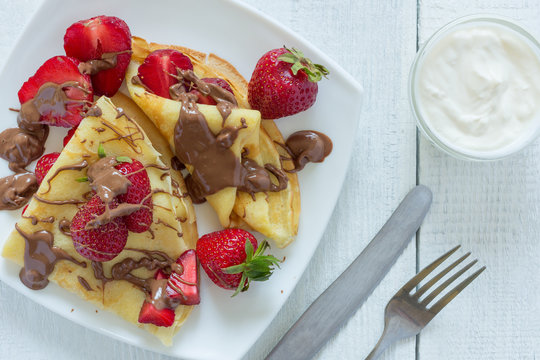 Pancakes with strawberries drizzled with chocolate. On a white wooden background. The view from the top.