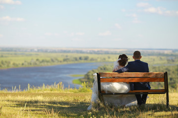 Fototapeta premium Young wedding romantic couple sitting on wooden bench outdoor on river background.