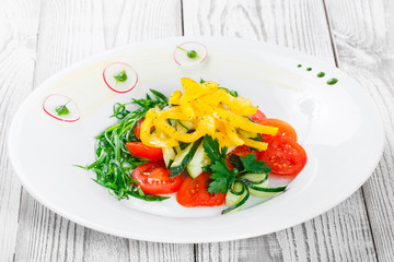 Fresh salad with cherry tomatoes, cucumber, radish, sweet pepper and onion in a plate on wooden background close up. Top view
