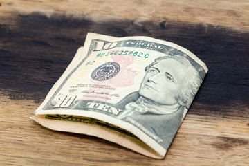 A folded ten USA dollar note on a wooden background. This image can be used to represent payment.