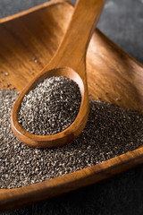 Raw unprocessed black chia seeds on wooden spoon on chia seeds