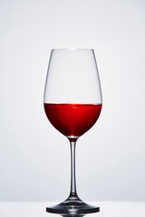 Halffull wine pure wine glass with red wine against light background with reflection.