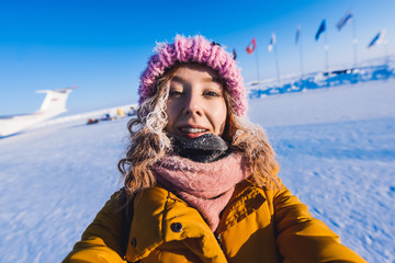 Fototapeta na wymiar Close-up of a girl in a yellow down jacket pink knitted cap with red hair beautiful young hair in a hoarfrost in the background of the camp Barneo on a snowy north pole in winter