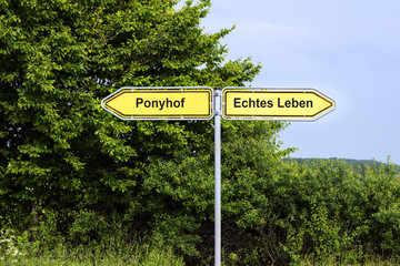 Yellow road signs pointing in opposite directions with german text Ponyhof,  Echtes Leben, that means Pony Farm, Real Life, green bushes and a blue sky in the background