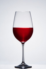 Fragile elegant wineglass of red wine standing against light background.