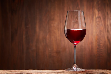 Red wine in the pure elegant wineglass standing on a wooden stand against wooden background.