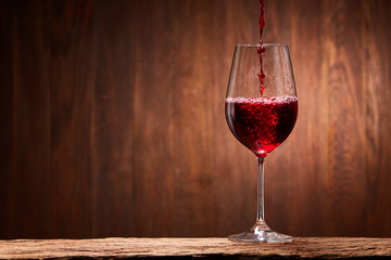 Tasty red wine poured in the elegant glass standing on the wooden stand against wooden wall background.