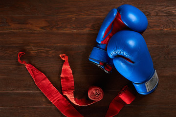 Top view of blue and red boxing gloves and bandage on wooden plank background.