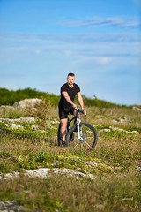 Attractive sportsman riding bike on rocky trail against sky with clouds.