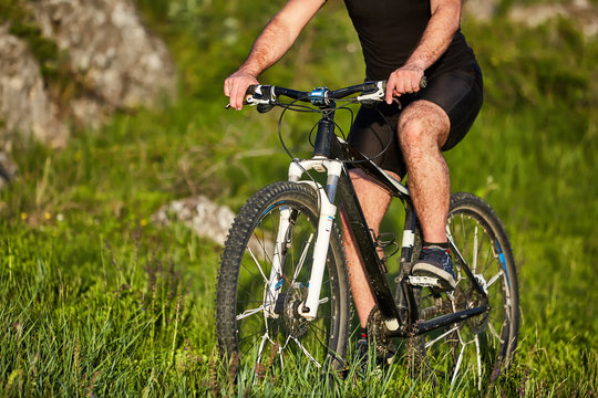 Close-up of the wheel of a bicycle and legs of the cyclist on the meadow.