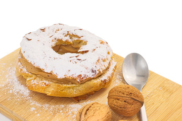 Paris Brest (French dessert choux pastry and praline cream) on wood board and walnuts on white background