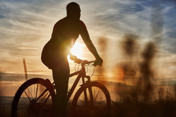Fototapeta na wymiar Silhouette of cyclist standing with mountain bike on the hill at sunset.