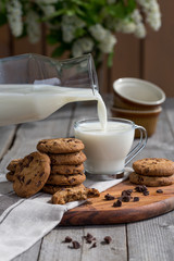 Chocolate chip cookies with milk on old rustic wooden table. Milk pouring.