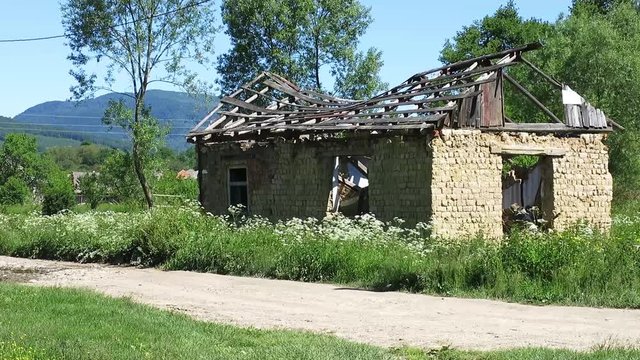 A ruined house near a dirt road in the background of a mountainous area. Woman with daughter passing by destroyed old house.