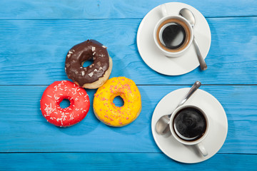 Obraz na płótnie Canvas Two cups with coffee and donuts on a blue wooden table
