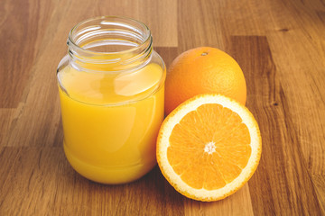 Naklejka na ściany i meble Fresh orange juice in the glass next to the orange slices on wooden table