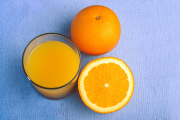Fresh orange juice in the glass next to the orange slices on blue wooden table