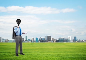 Camera headed man standing on green grass against modern cityscape
