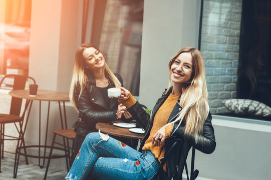 Two beautiful young women in fashion clothes having rest talking and drinking coffee in restaurant outdoor. concept of friendship lifestyle fashion. sunny day for walk with friends and have a fun.